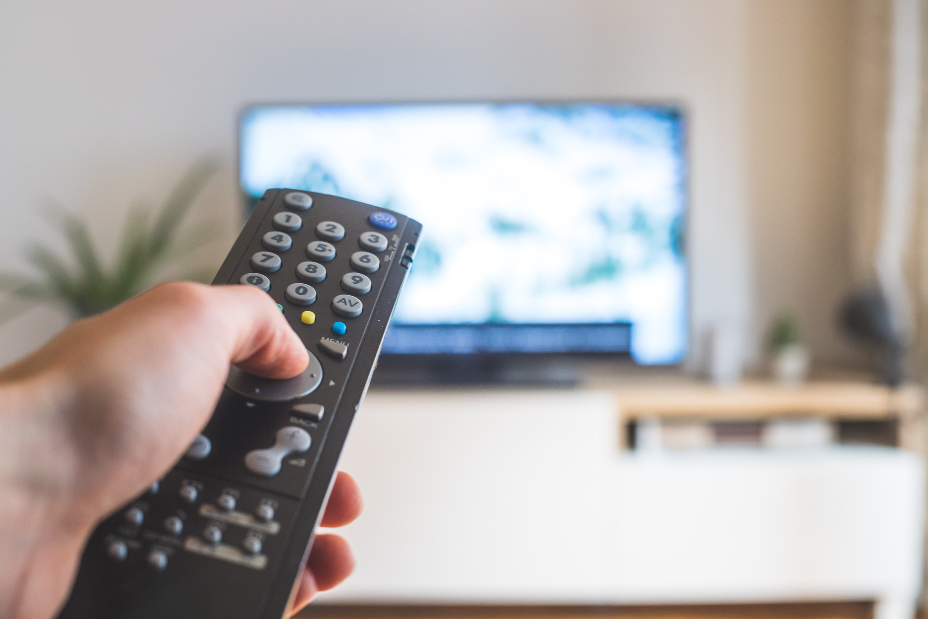 Male hand is holding TV remote control, streaming on a smart TV.